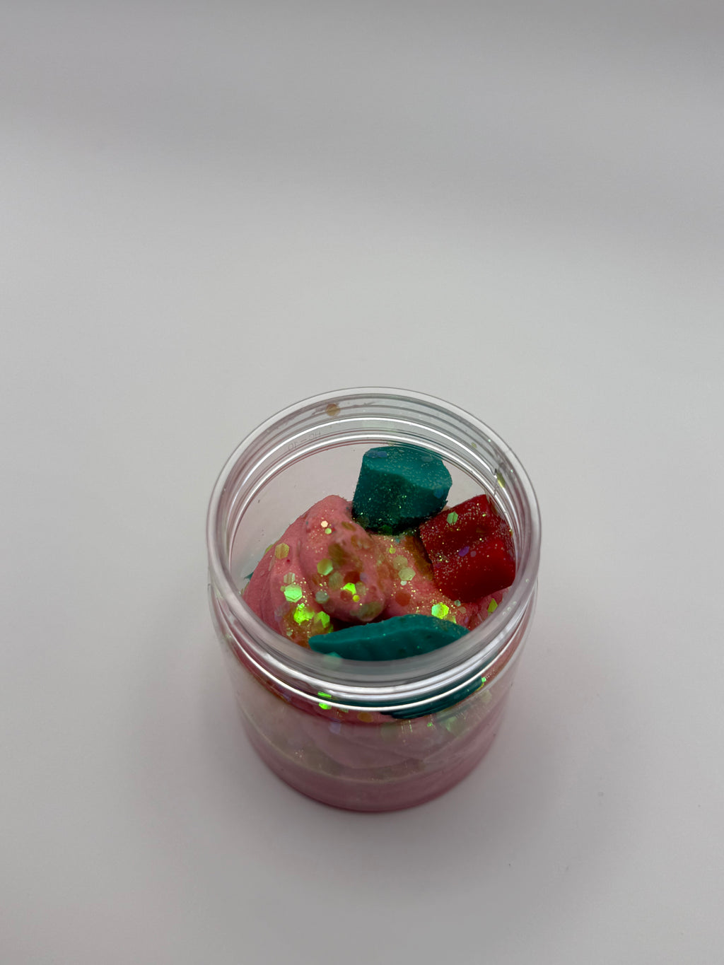 Small glass jar filled with colorful glittery stones on a light gray background