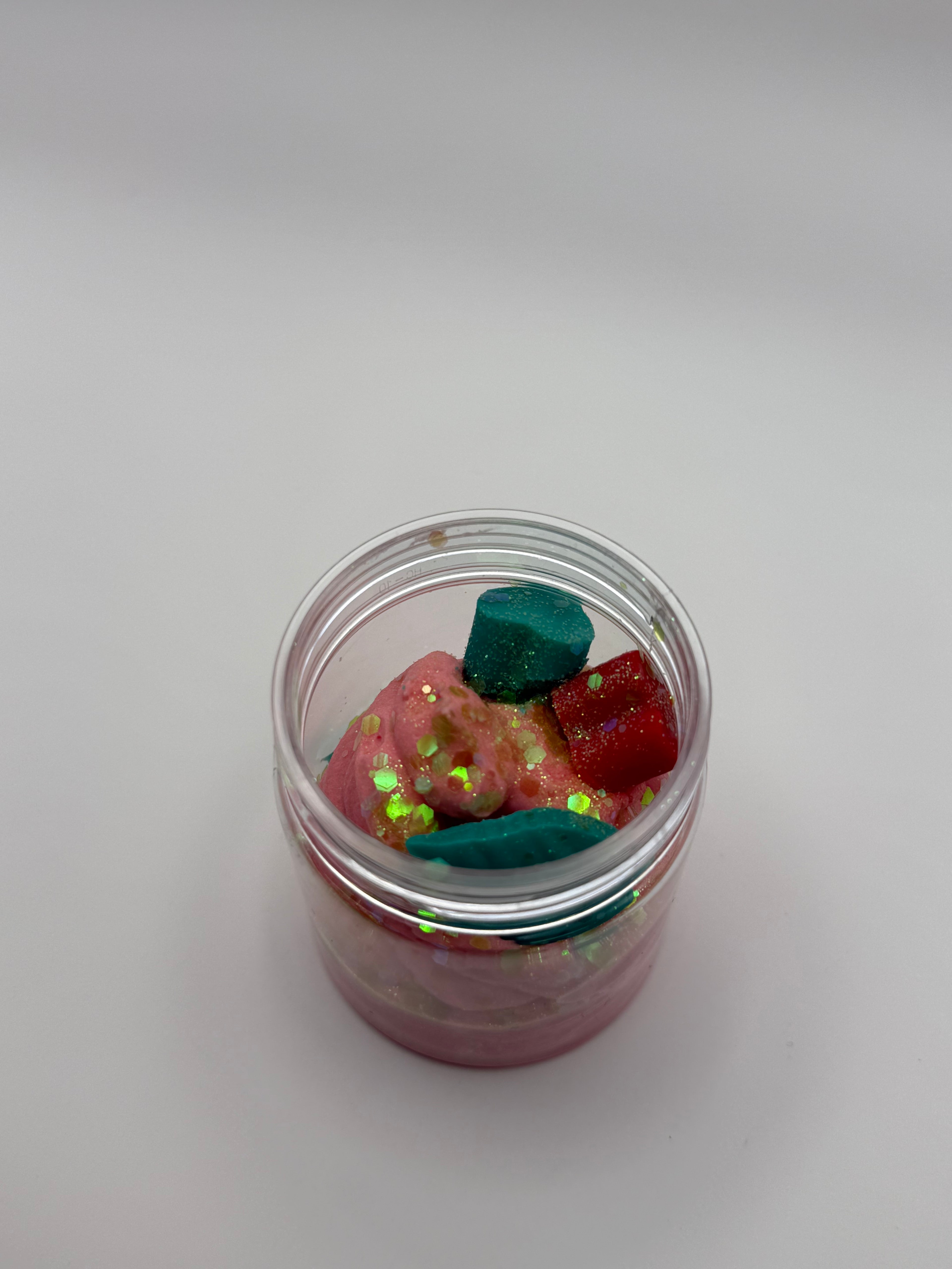 Small glass jar filled with colorful glittery stones on a light gray background